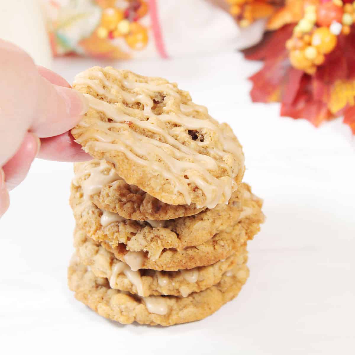 Lifting Maple Oatmeal Cookie off stack of iced cookies.
