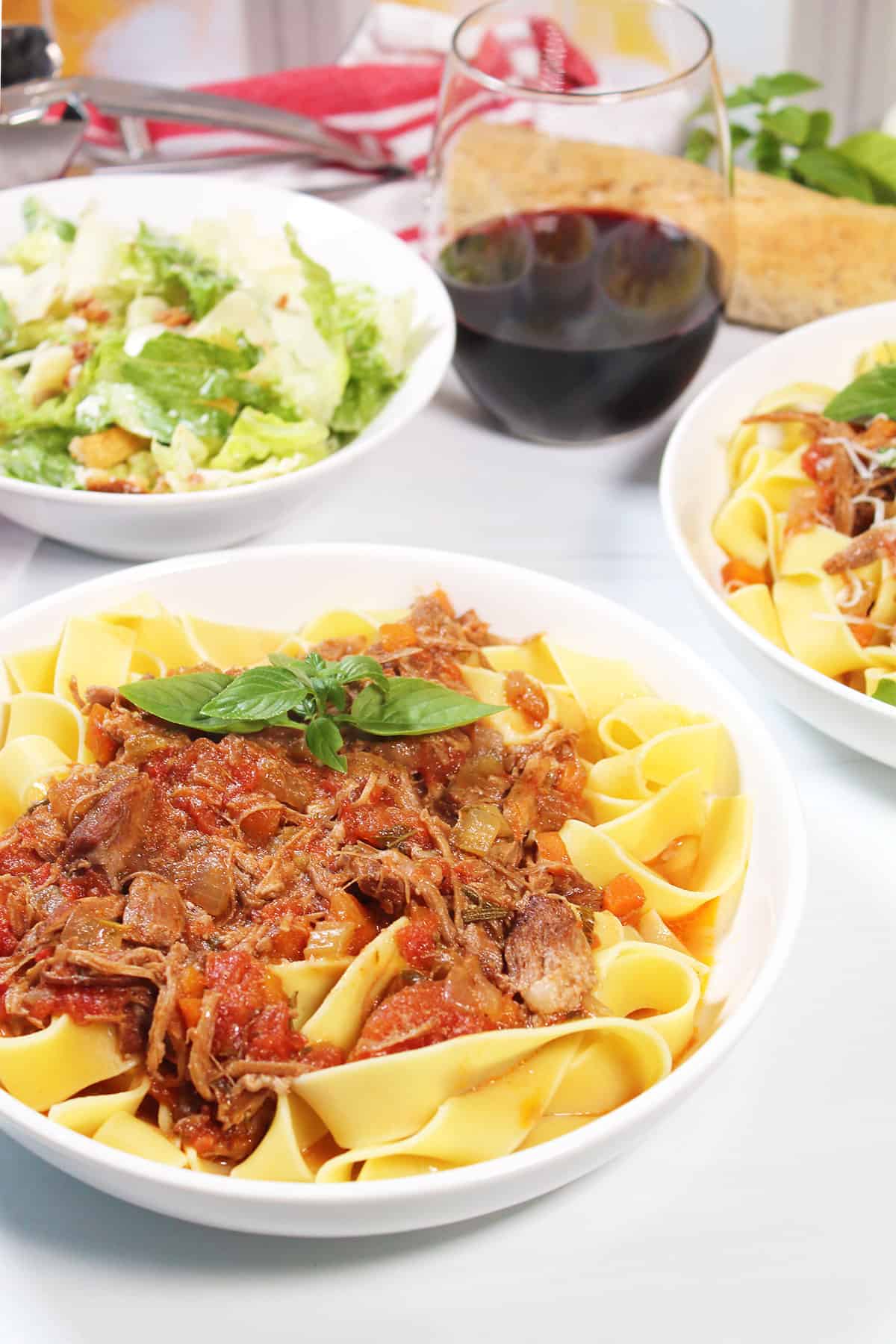 Bowl of Instant Pot Pork Ragu with salad and glass of wine.