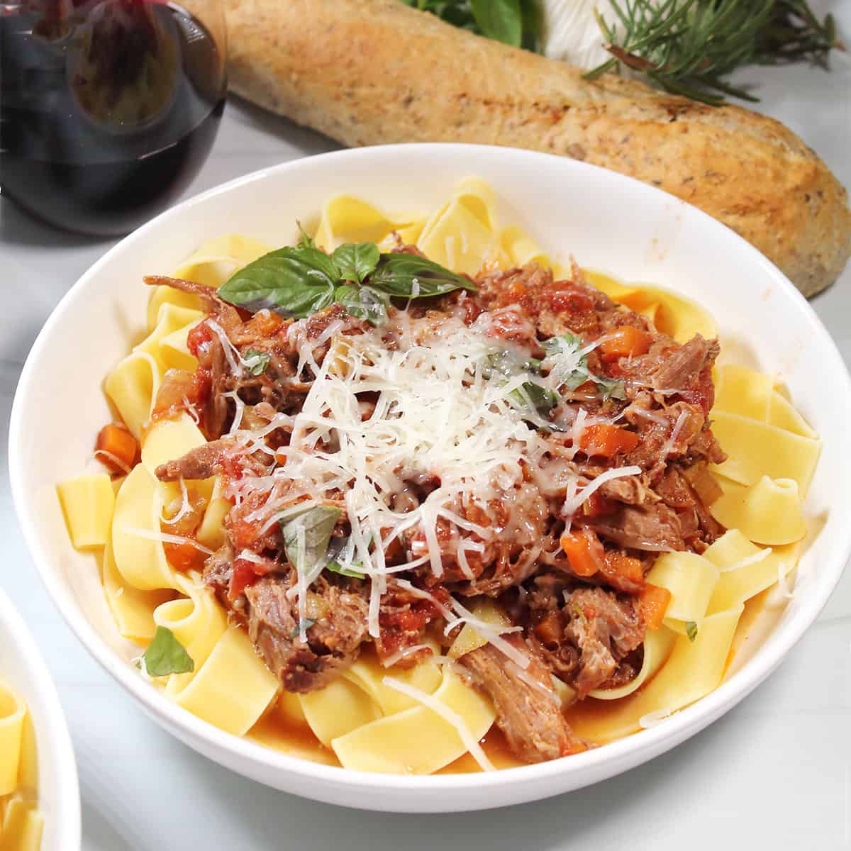 Bowlful of pork ragu with pasta topped with Parmesan cheese.