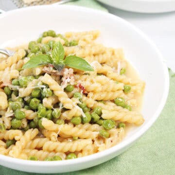 Closeup of Pasta e Piselli in bowl with Parmesan and basil garnish.