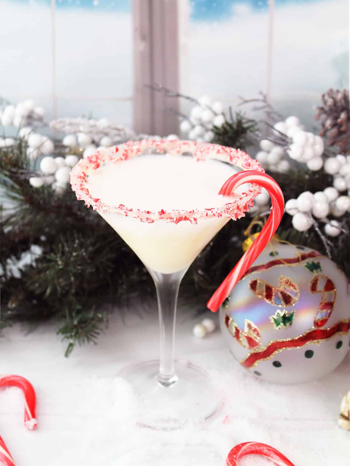 Single candy cane martini by frosted window.