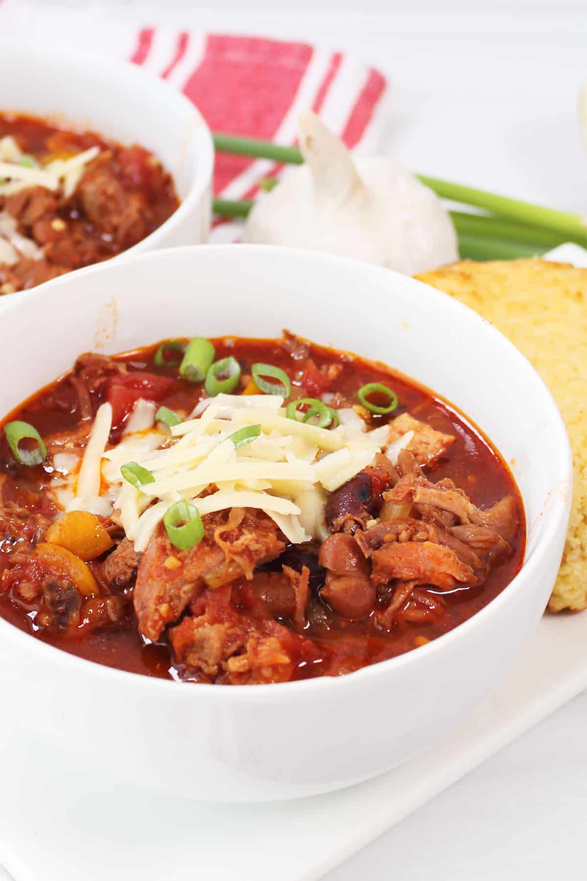 Pulled Pork Chili in bowl with cheese and green onion garnish.