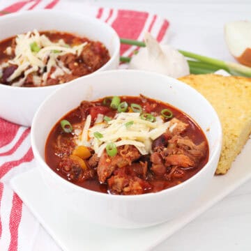 Two bowls of pulled pork chili with cheese and green onions on top.