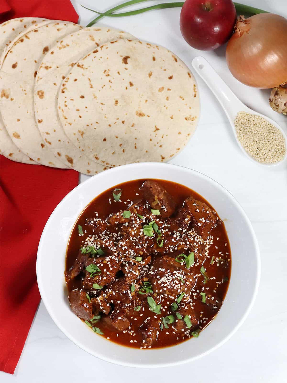 Serving bowl of finished Korean Beef with garnish of green onions and sesame seeds.