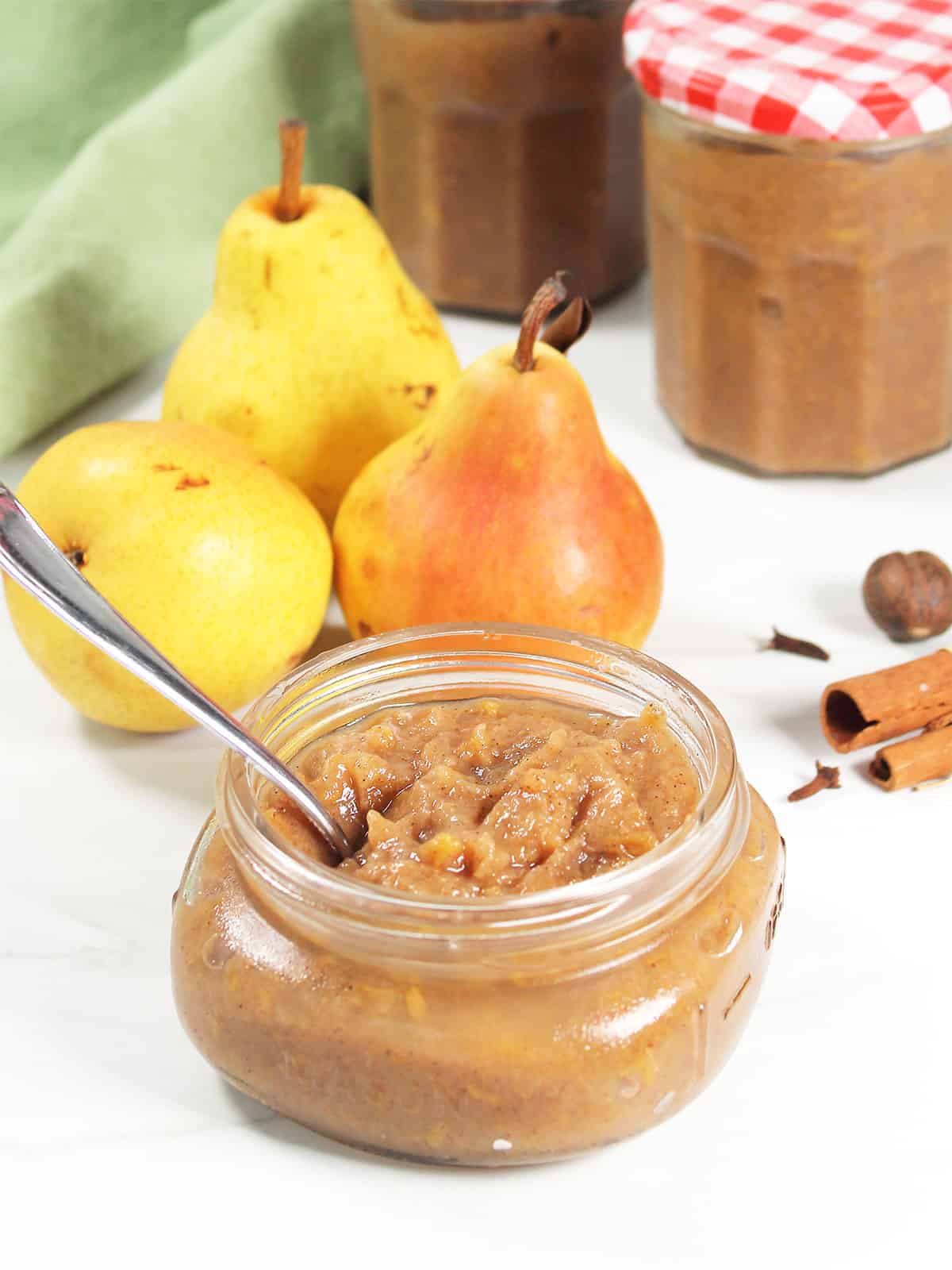Pear Butter in a jar with a spoon in it with pears behind it.