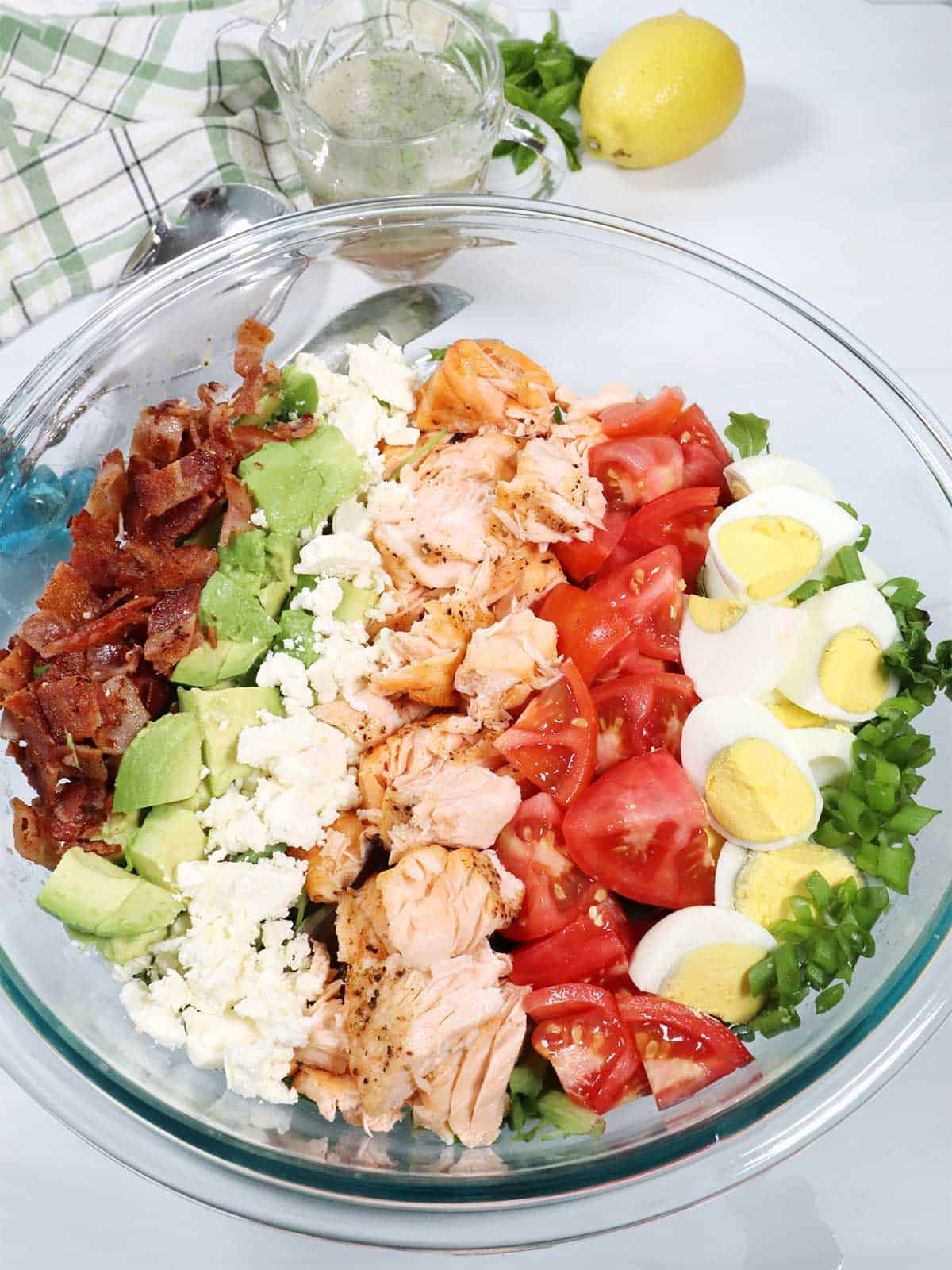 Closeup of layered Salmon Cobb Salad with vinaigrette in back.